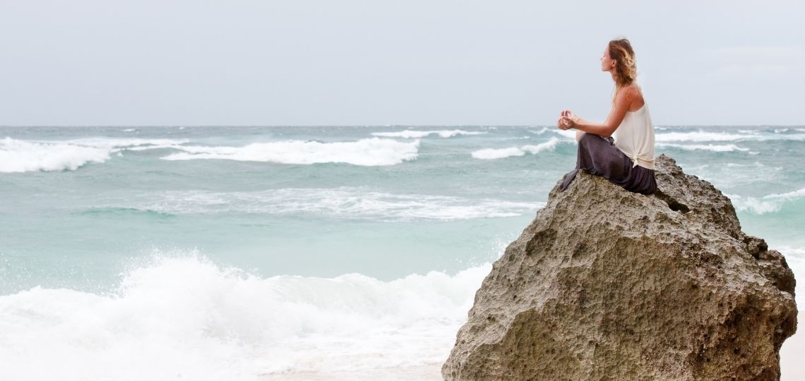 Girl practicing mindfulness by meditating in a beach