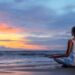 A woman meditating in the beach with a great sunset