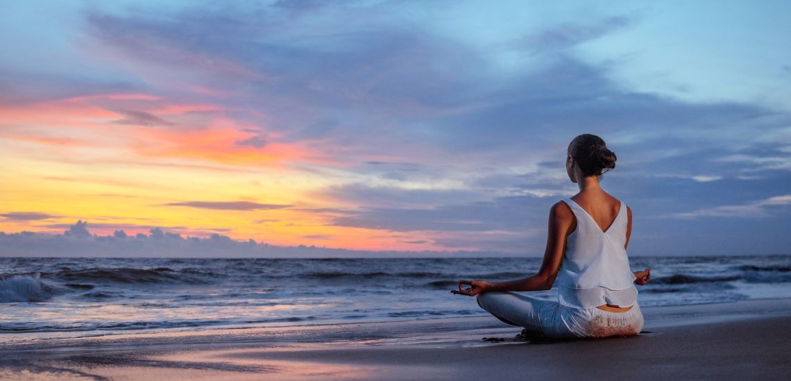 A woman meditating in the beach with a great sunset